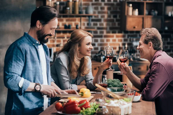 Amigos bebiendo vino mientras cocinan la cena - foto de stock