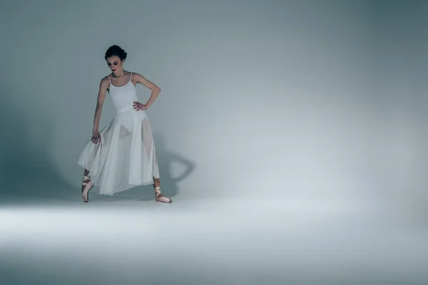 Елегантна балерина в білій сукні, що розтягується в студії — стокове фото