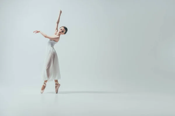 Приваблива балерина в білій сукні танцює в студії, ізольована на білому — стокове фото