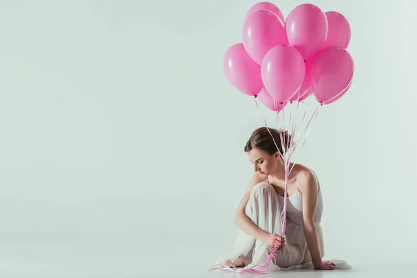 Балетна танцівниця в білій сукні, сидить з рожевими кульками, ізольована на білому — стокове фото