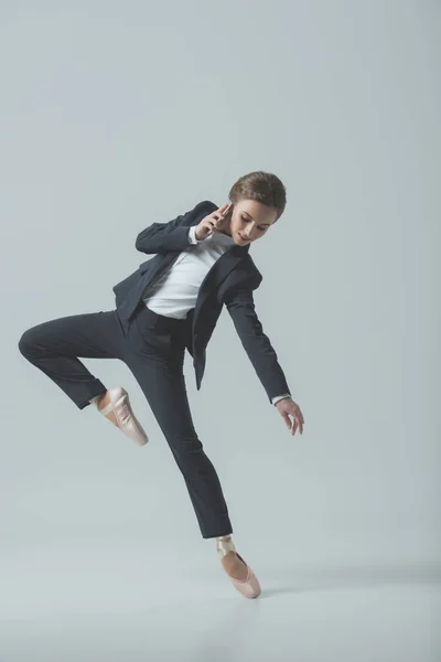 Femme d'affaires en costume et chaussures de ballet dansant et parlant sur smartphone, isolée sur gris — Photo de stock