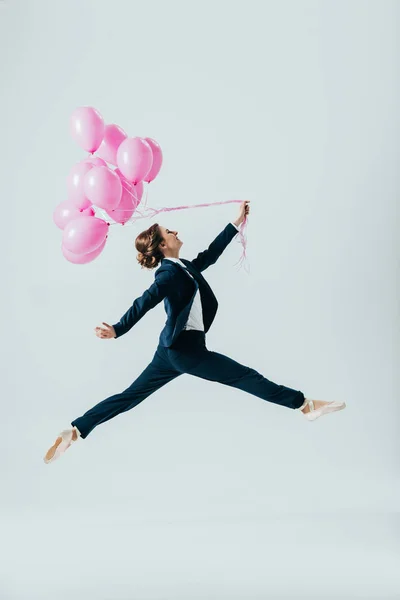 Donna d'affari in giacca e cravatta e ballerine che salta con palloncini rosa, isolata su grigio — Foto stock