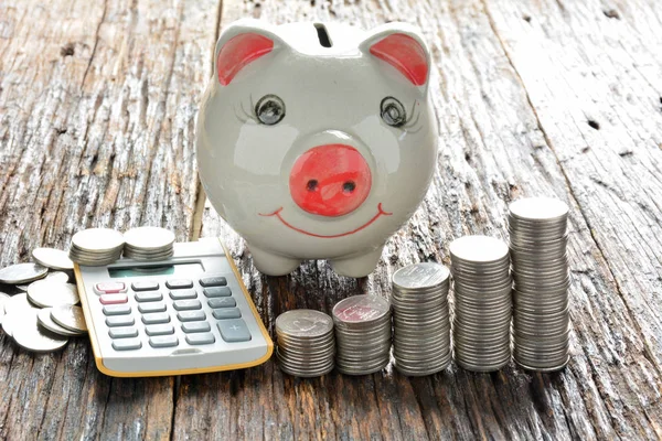 Monedas de pila, calculadora y alcancía en mesa de madera — Foto de Stock