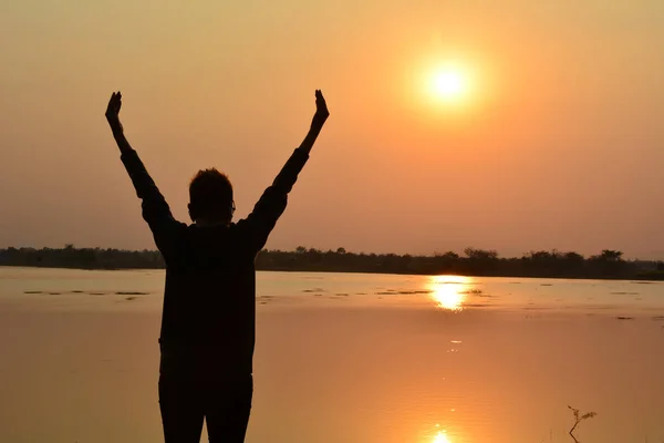 Женщина подняла руку у озера под небом и солнечным вечером — стоковое фото