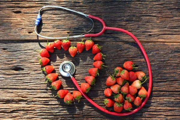 Stethoskop und Erdbeerherz für Gesunde auf alter Holzrinde — Stockfoto