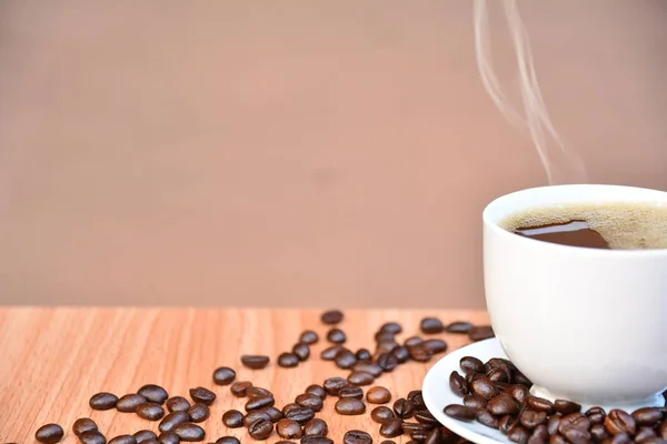 Grãos de café e café em copo branco na mesa de madeira — Fotografia de Stock
