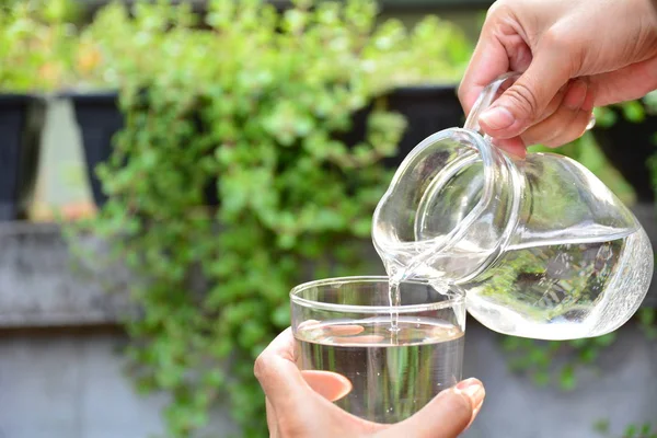 Pouring water from jar into glass on nature background — Stock Photo, Image