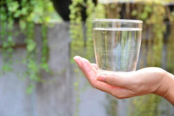 Las manos sostienen el vaso y el agua en vidrio sobre el fondo de la naturaleza — Foto de Stock