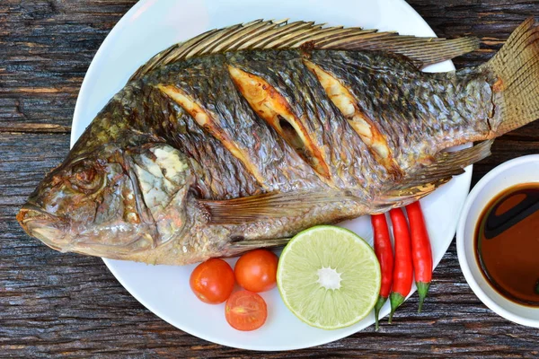 Biber biber, limon ve domates ile beyaz plaka üzerinde ızgara balık 
