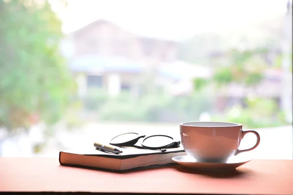 Taza de café con libro, pluma y vasos en una mesa de madera — Foto de Stock