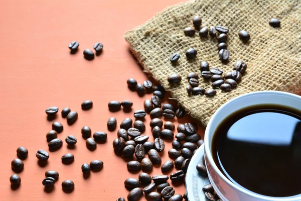Xícara de café com grãos de café e saco em um fundo laranja — Fotografia de Stock