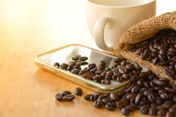 Kaffebönor i säcken sätta på den smarta telefonen med kaffekopp — Stockfoto