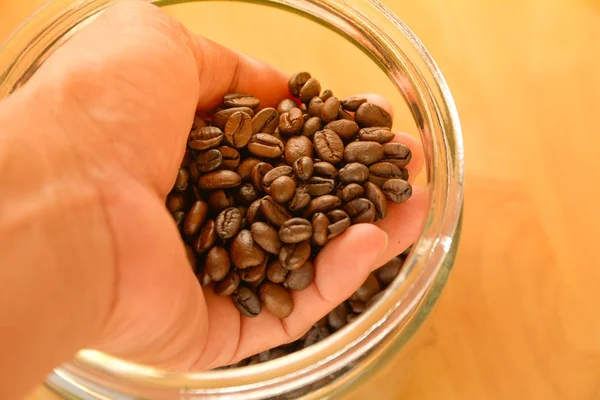 Kaffebönor i händer och släppa i burken på träbord. — Stockfoto