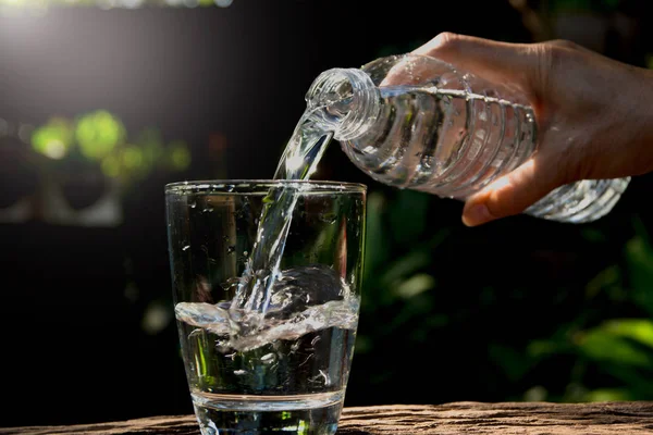 Hembra mano verter agua de botella a vidrio en la naturaleza backgro — Foto de Stock