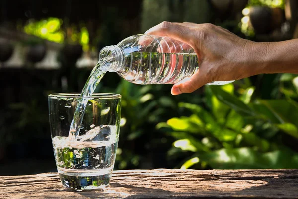 Weibliche Hand gießt Wasser von Flasche zu Glas auf Natur-Backgro — Stockfoto