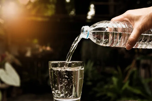 Hembra mano verter agua de botella a vidrio en la naturaleza backgro — Foto de Stock