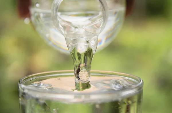 Persona que vierte agua de la botella al vidrio sobre el fondo de la naturaleza — Foto de Stock