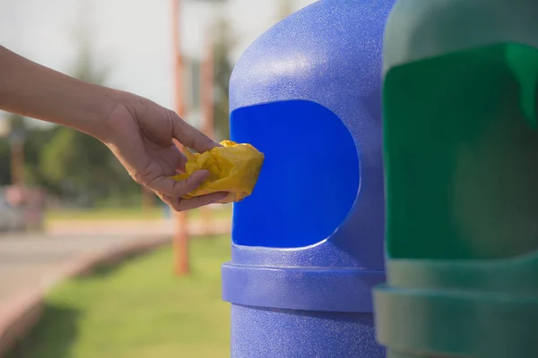 Female hand throwing crumpled yellow plastic into blue plastic trashcan. — Stock Photo, Image