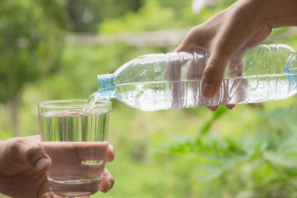 Hembra mano verter agua de la botella al vidrio sobre fondo de la naturaleza — Foto de Stock