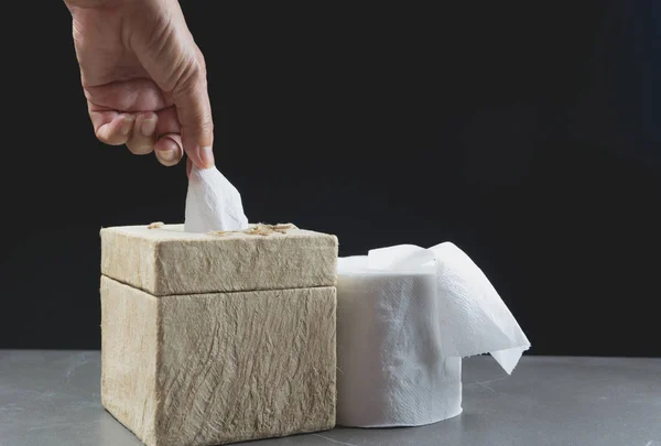 Close-up image hand pull the toilet papers roll in box with toilet papers roll on the table with dark background.