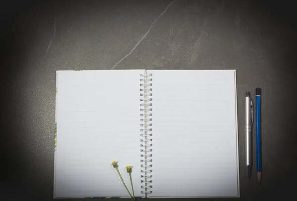 Вид зверху на відкриту книгу. Книга відкрита, з ручкою і квіткою на фоні темного тону столу . — стокове фото