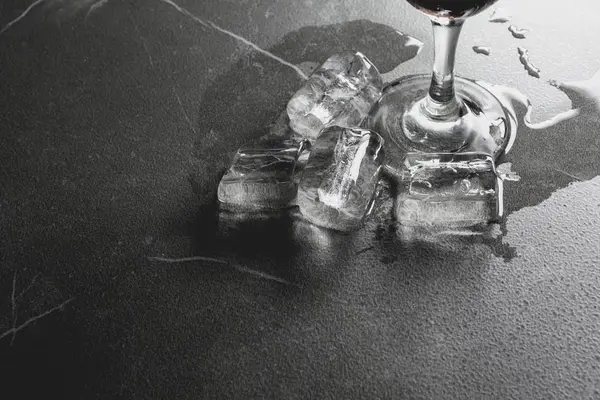Проливание воды из стакана воды со льдом на темном столе . — стоковое фото