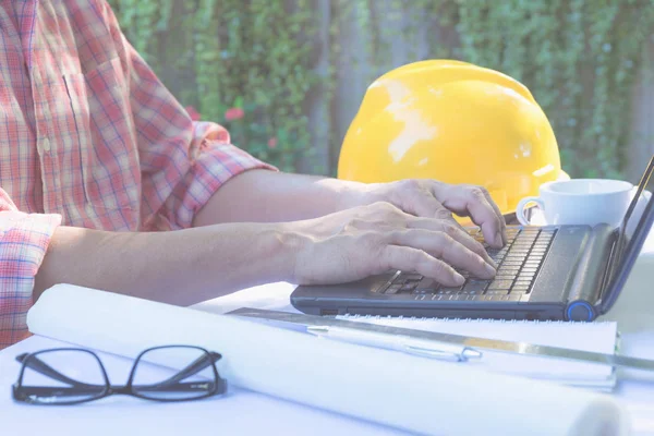 Masada beyaz kask, dizüstü bilgisayar ve kahve fincanıyla çalışmak için dizüstü bilgisayar kullanan mimar mühendisi..
