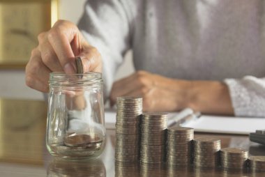 Kadın süreci ve damla yığını sikke ve hesap makinesi ile cam içine para. Tablo üzerinde çalışan kadın.