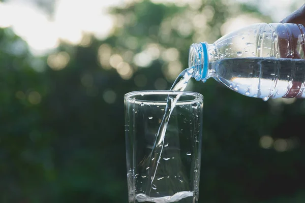 Hembra mano verter agua de la botella al vidrio sobre fondo de la naturaleza — Foto de Stock