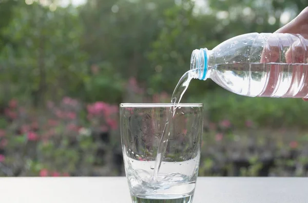 Hembra mano verter agua de la botella al vidrio sobre fondo de la naturaleza — Foto de Stock