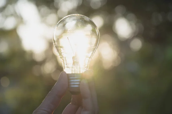 Ruka člověka drží žárovku za nápad nebo úspěch nebo solární energetické koncepce. — Stock fotografie