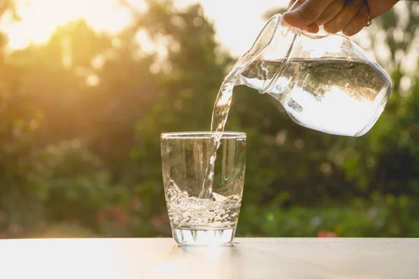 Person pouring water from pitcher to glass on nature background — Stock Photo, Image