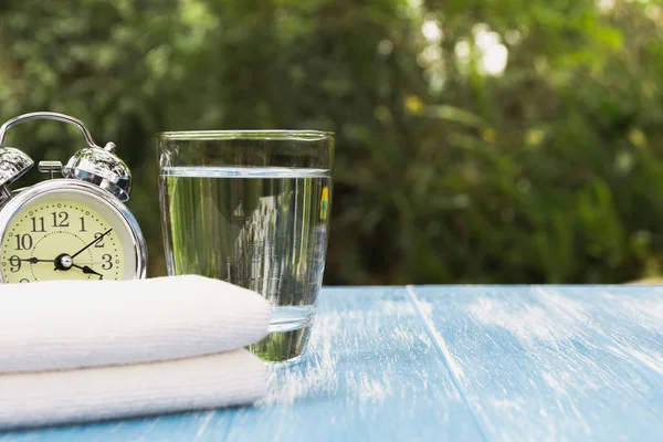 Agua en vidrio con despertador y pañuelo sobre fondo natural . — Foto de Stock