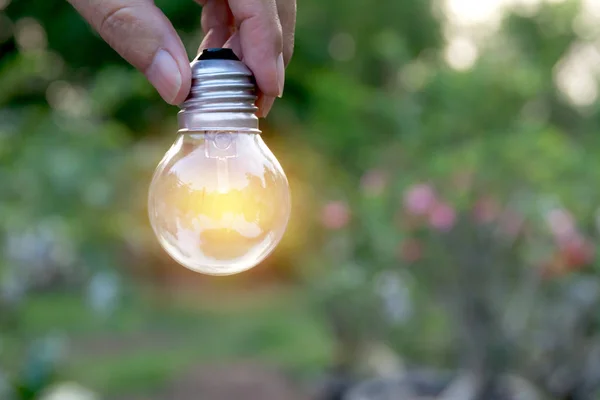 Mano sosteniendo bombillas con resplandor en el suelo. Idea, creatividad y ahorro de energía con el concepto de bombillas . — Foto de Stock