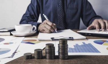 Finans ve muhasebe kavramı için para yığınıyla çalışan ve not defteri üzerine yazan bir iş adamı..