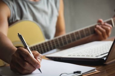 Kalem tutan ve şarkı sözlerini kağıda yazan besteci. Akustik gitar çalan müzisyen..