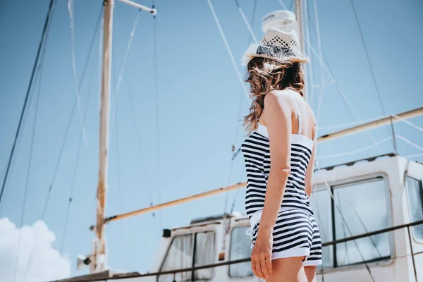 Woman in striped clothes standing near yacht in sunny summer day.