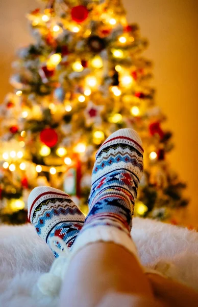 Frauenfüße in Wollsocken am Weihnachtsbaum. — Stockfoto