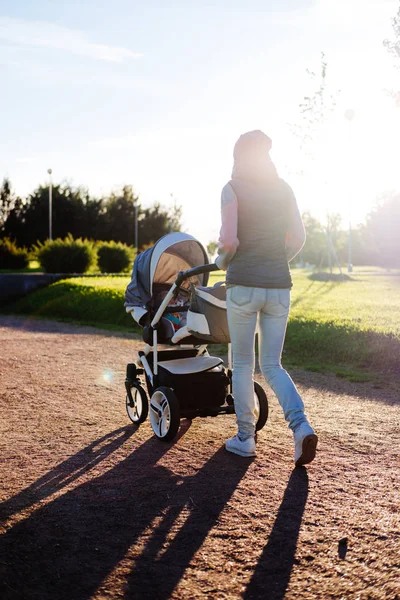 Молода мати з дитячою коляскою ходить у парку. Концепція сім'ї, дитини та батьківства . — стокове фото