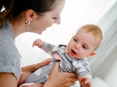 Mutlu gülümseyen anne ve bebek evde yatakta oynuyor. Mutlu aile eğleniyor..