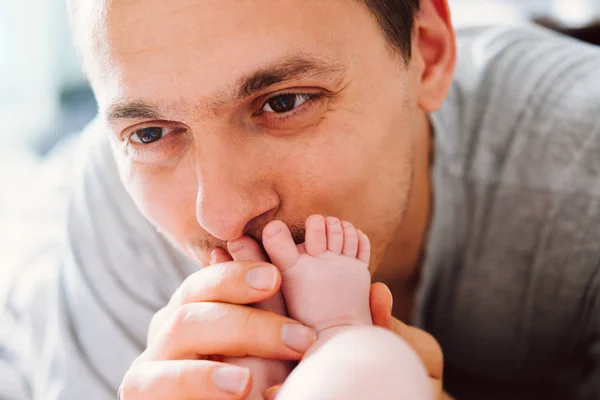Feliz joven padre mirando con ternura a su bebé y besándole los pies . — Foto de Stock