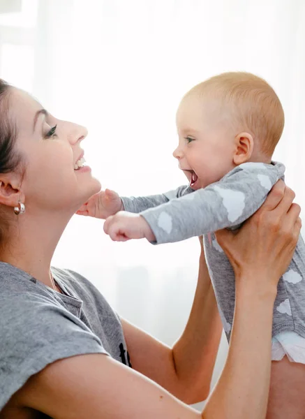 Feliz madre sonriente y bebé jugando en la cama en casa. Familia feliz divirtiéndose . — Foto de Stock