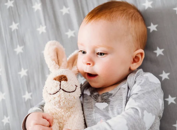 Gelukkig lachende babymeisje met haar speelgoed op het bed. — Stockfoto