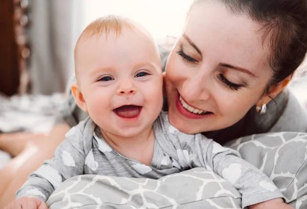 Feliz madre sonriente y bebé jugando en la cama en casa. Familia feliz divirtiéndose . —  Fotos de Stock