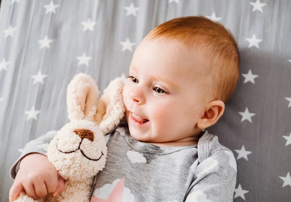 Gelukkig lachende babymeisje met haar speelgoed op het bed. — Stockfoto