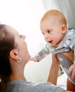 Mutlu gülümseyen anne ve bebek evde yatakta oynuyor. Mutlu aile eğleniyor..