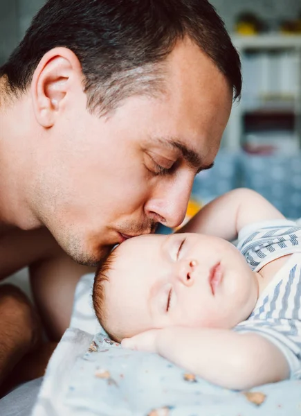 Feliz joven padre mirando con ternura a su niña dormida y besándola . — Foto de Stock