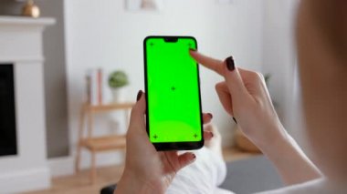 Evde koltukta oturan akıllı telefonu kullanan genç bir kadın..