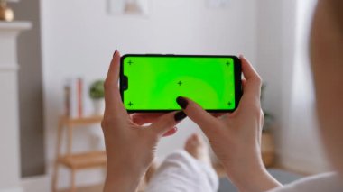Evde koltukta oturan akıllı telefonu kullanan genç bir kadın..