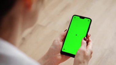 Evde koltukta oturan akıllı telefonu kullanan genç bir kadın..